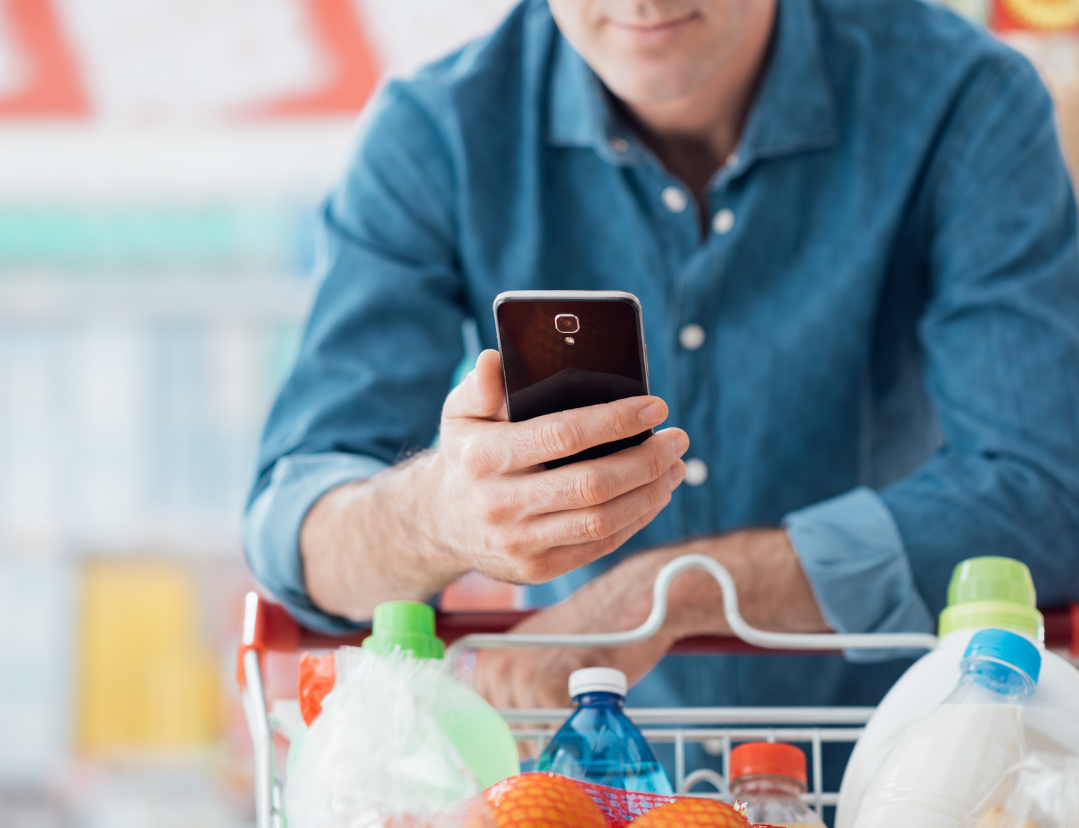 Uomo che spinge un carrello della spesa tenendo il telefono in mano