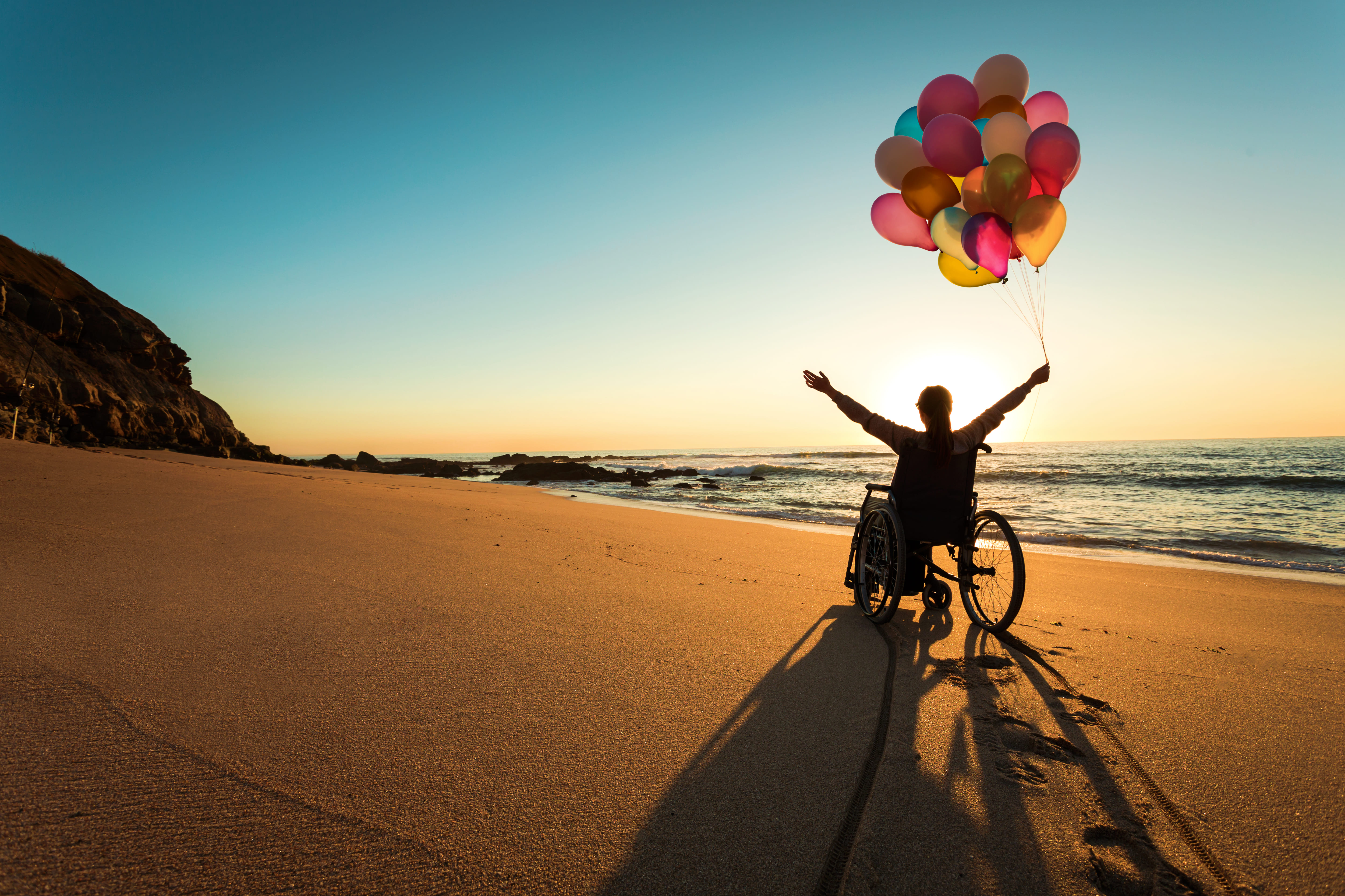 Una persona in sedia a rotelle in spiaggia fa volare dei palloncini