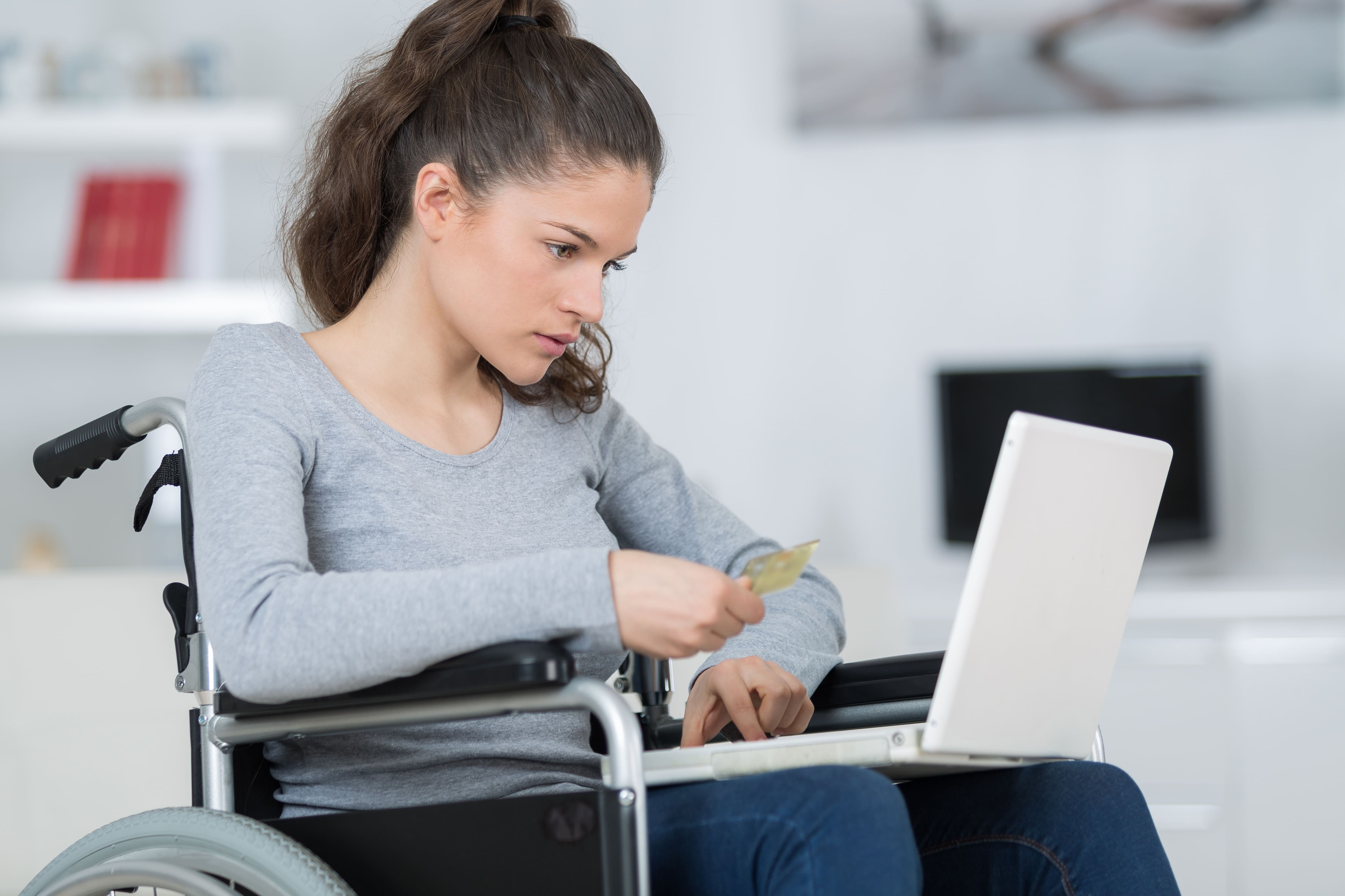 Una persona con disabilità motoria agita una carta di credito davanti a un pc