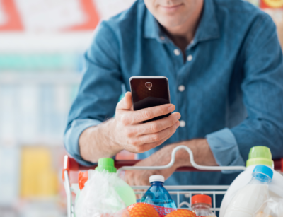 Un uomo spinge un carrello della spesa mentre guarda il cellulare